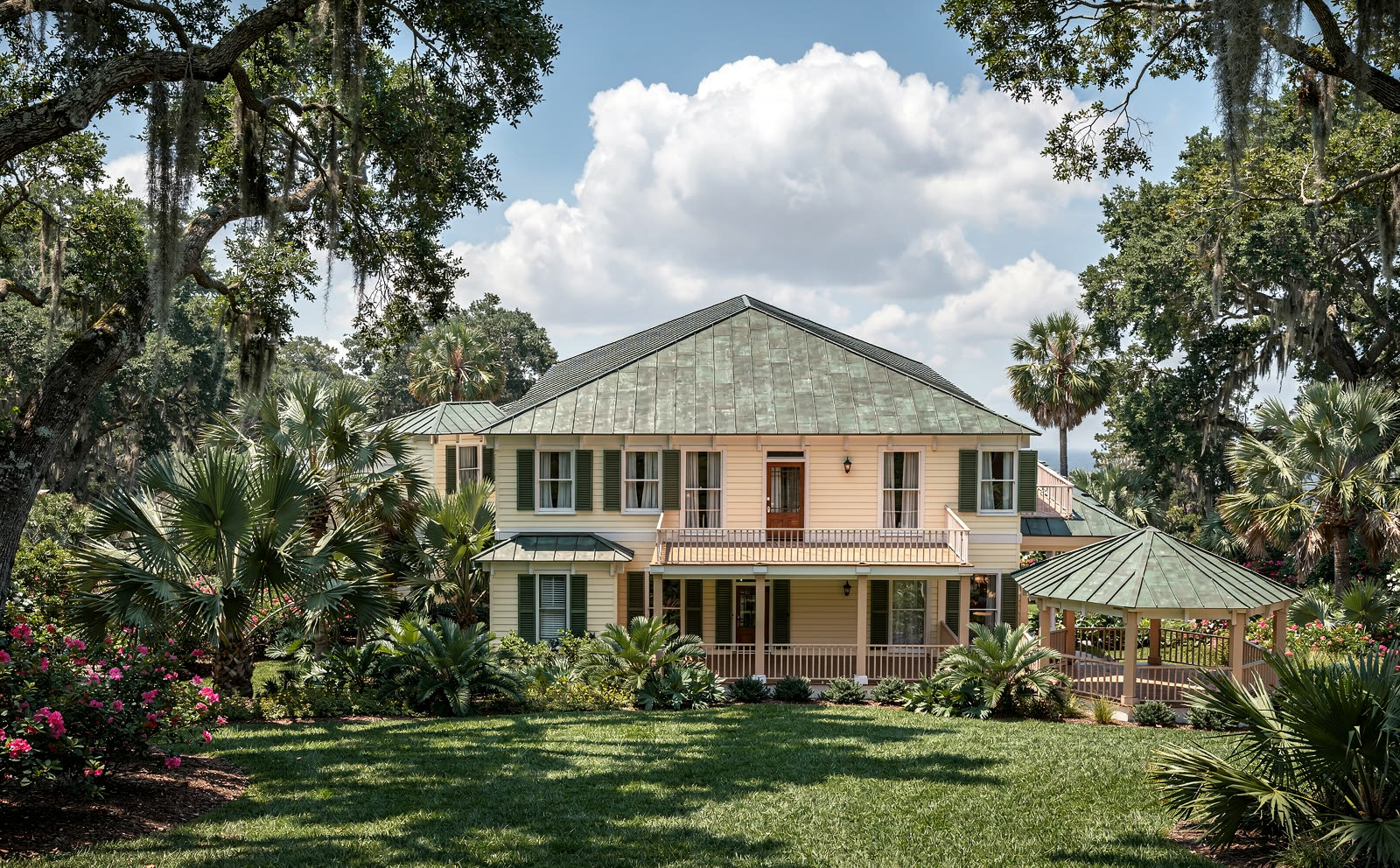 Photograph of the same house from the west: the gazebo end nearest
      the camera, the two storey porch running away to the right, palms and azalea beds against the foundation.